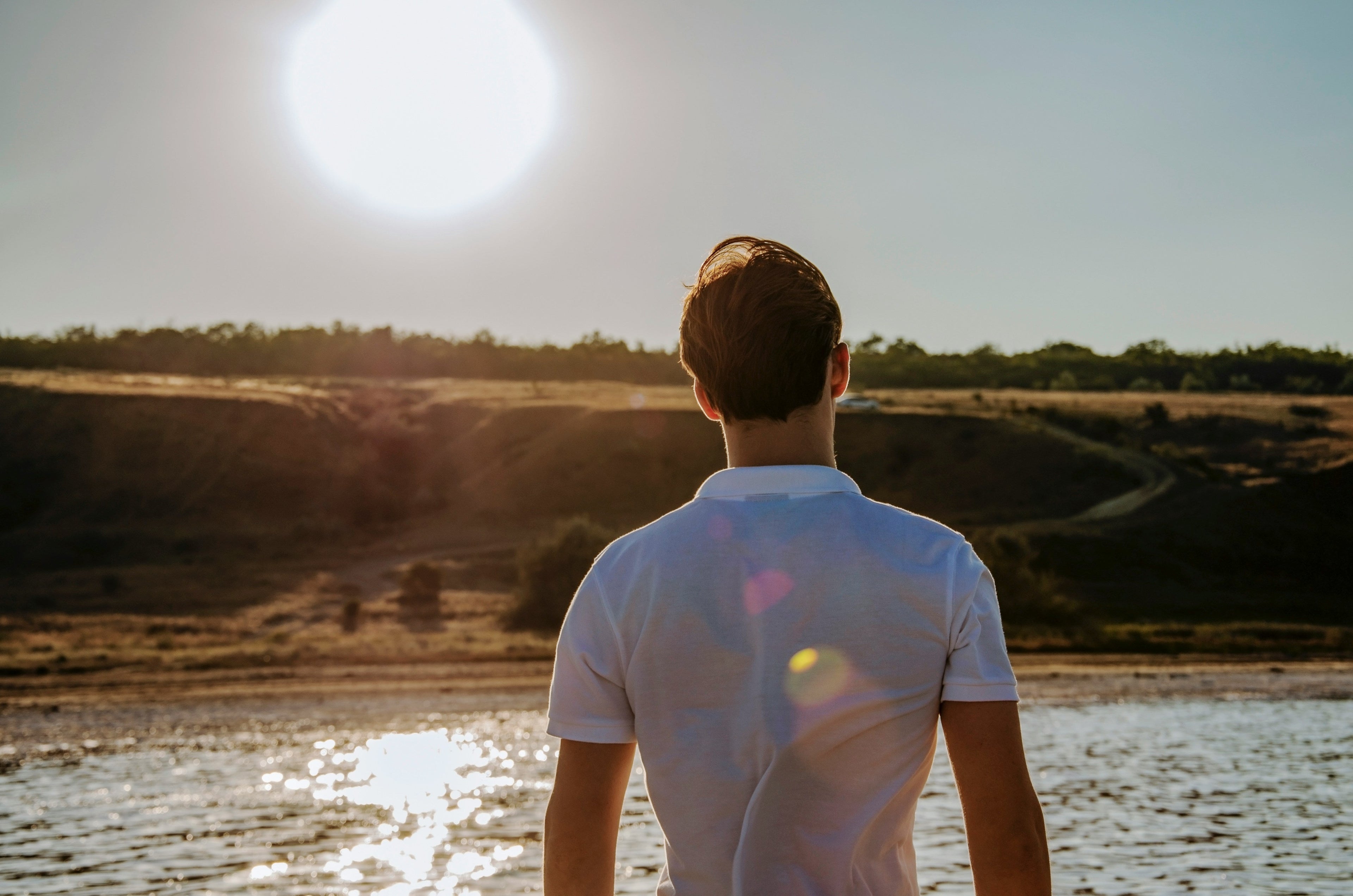 Man facing the sun, which is setting over a river